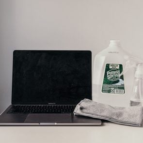 Open laptop on surface next to a poland spring gallon, spray bottle, and gray cloth