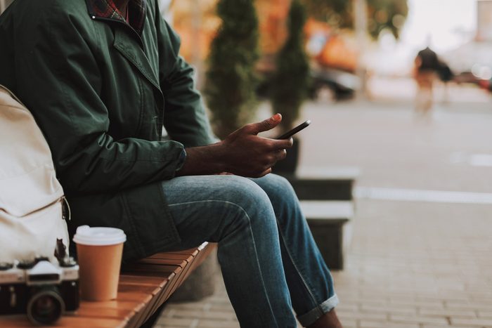 close up of man sitting on bench looking at smartphone