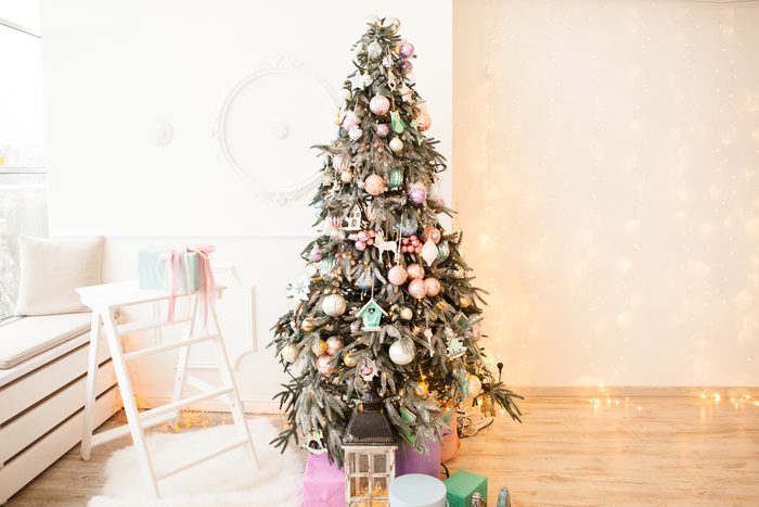 Christmas tree decorated with glass and wooden vintage toys and gift boxes in pastel colors near window in light interior with lights garland on wall