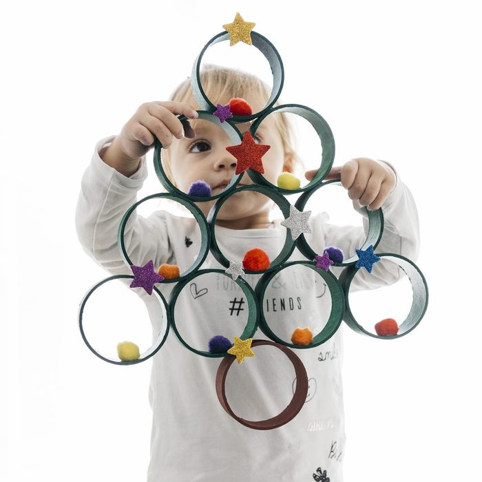Little child holding a Christmas tree made with painted cardboard rolls and accessories