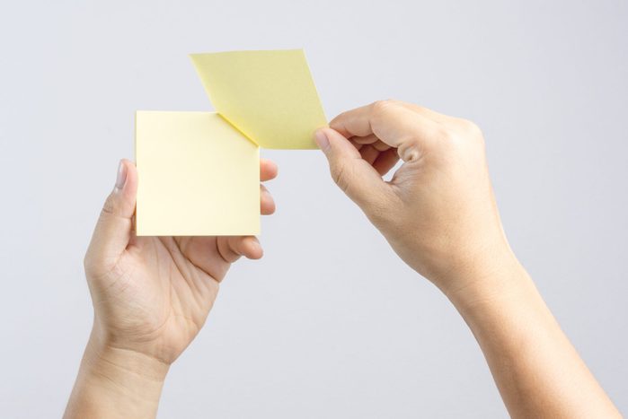 Close-Up Of Cropped Hands Holding Adhesive Notes Against Gray Background