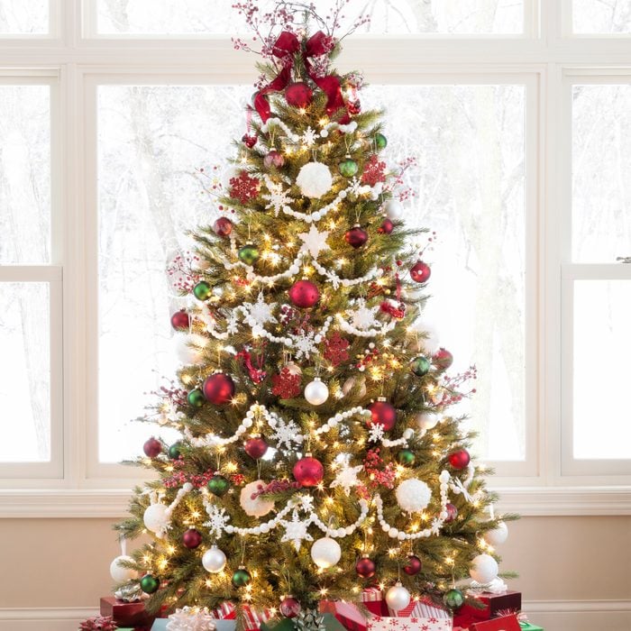 Christmas tree decorated in red, white and green with gifts against a large picture window and a wintery outdoor scene.