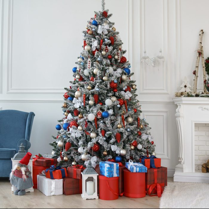 Decorated Christmas tree and red gift boxes beside decorated white fireplace