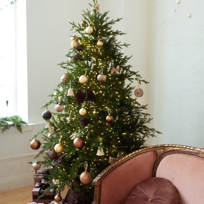 Pastel maroon sofa near e beautiful decorated Christmas tree. Balls ornaments garlands in rose gold brown style decoration on Christmas tree.