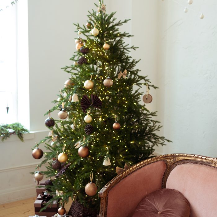 Pastel maroon sofa near e beautiful decorated Christmas tree. Balls ornaments garlands in rose gold brown style decoration on Christmas tree.