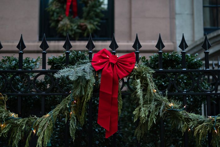 A closeup of a beautiful red holiday Christmas bow with lights and decorative pine branches on a fence in New York City.