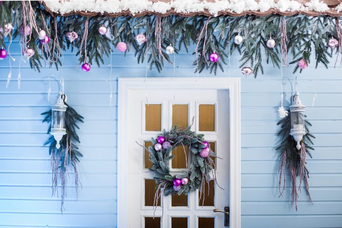 White door with hanging Christmas wreath under tiled roof decorated tree branches with ornaments and lights