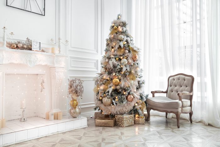 Classic white christmas interior with new year tree decorated. Fireplace with grey chair, clocks on the wall and presents under the tree