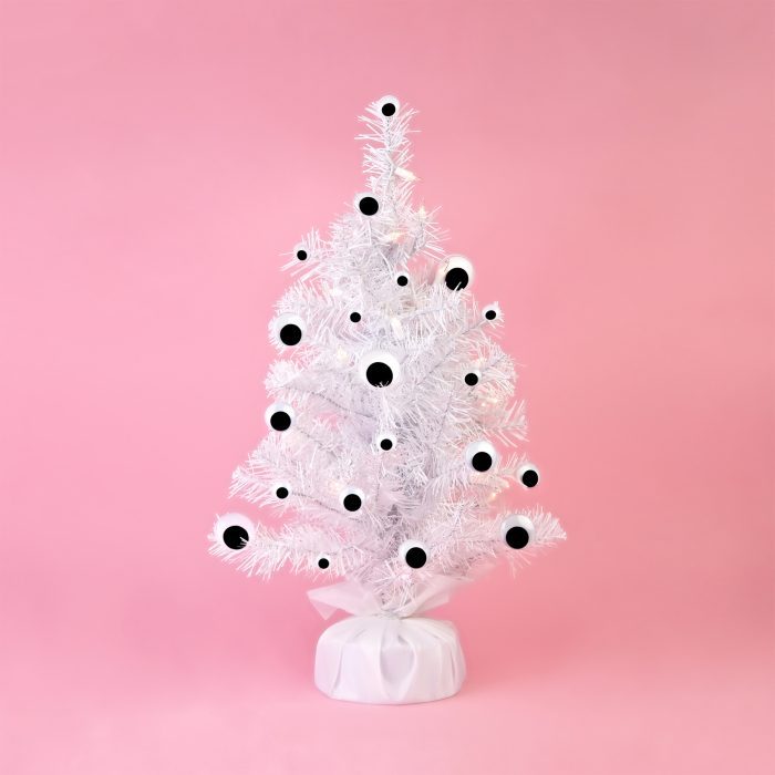 White tinsel Christmas tree decorated with google eyes on a pink background.