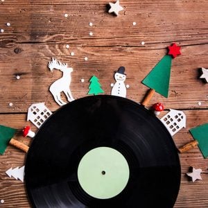 Flatlay of vinyl record with paper cutouts of Christmas trees and other Christmas items around the edge on a wood table background