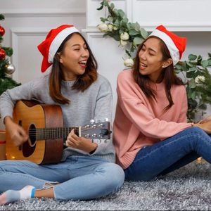 two girls with Christmas hats sitting on the living room floor singing and playing the guitar