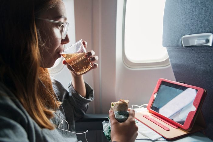 young woman eating and drinking on airplane
