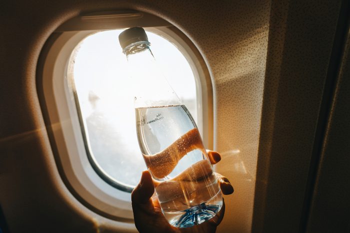 person holding bottle of water against airplane window