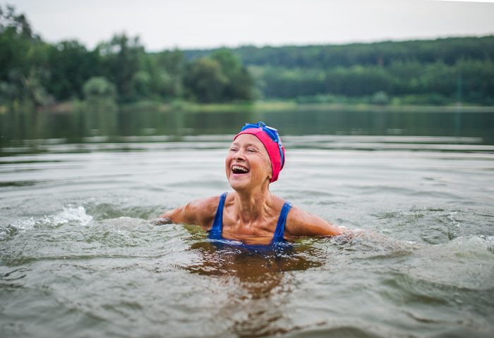 mature woman swimming in a lake on a cloudy day, smiling