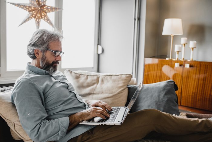 Mature man working on laptop on the couch at home