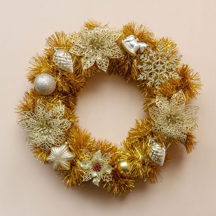 gold handmade christmas wreath from tinsel and baubles on pink background