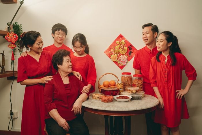 Asian family wearing red candidly standing around a table with Chinese New Year table before taking the family portrait photo
