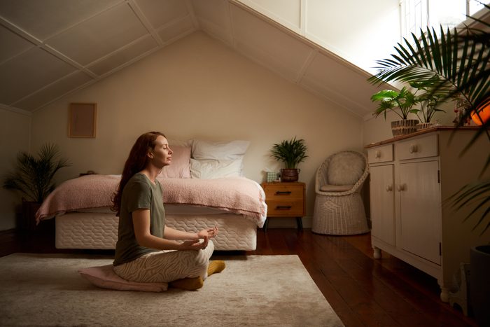 Young woman sitting on her bedroom floor and meditating