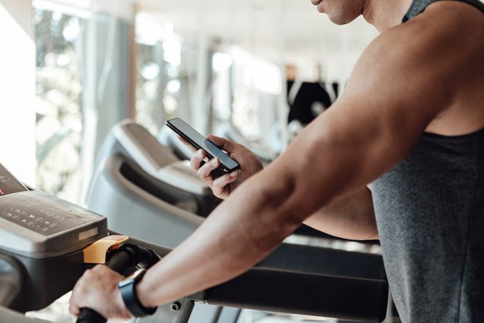young man looking at smartphone while on treadmill