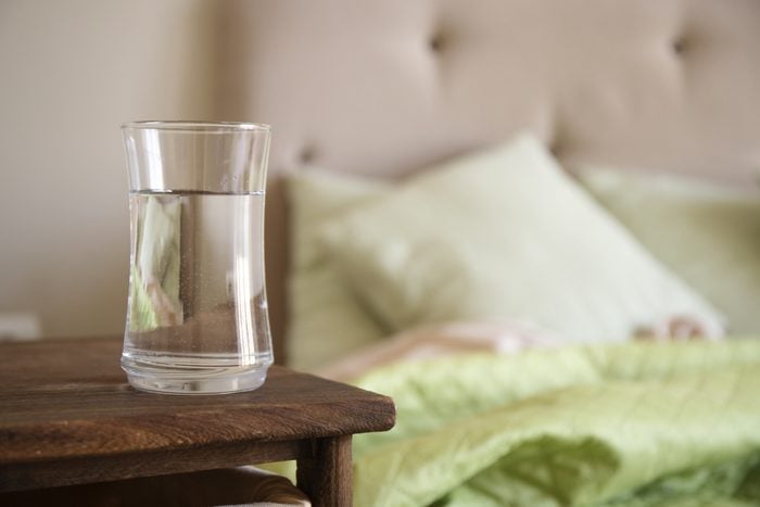 Glass with water on a wooden nightstand in bedroom