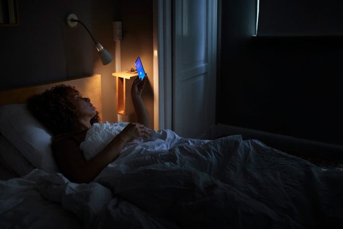 woman laying in bed at night looking at phone