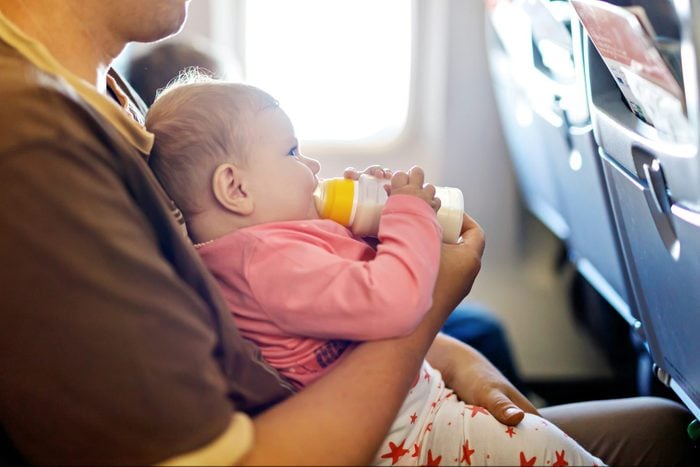 Father holding and feeding a bottle to his baby daughter during flight on airplane