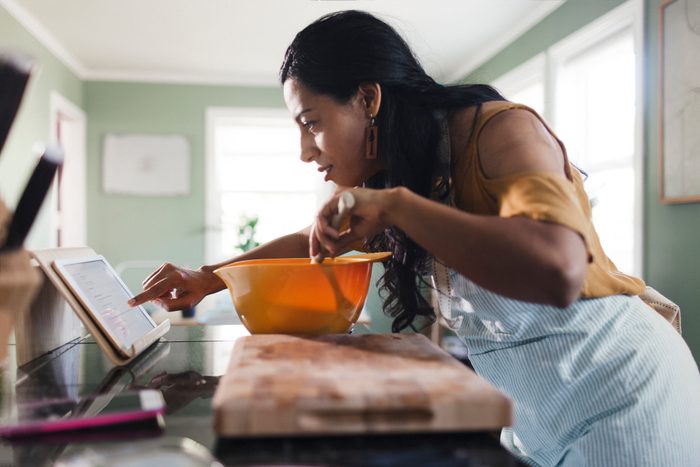 Side view of woman using tablet computer for recipe while preparing food in kitchen