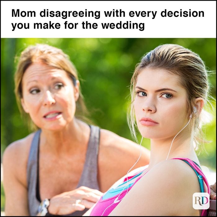 daughter ignoring her concerned mother. They are sitting on a park bench together. The daughter is blonde and is wearing a pink and blue shirt. Her mother is wearing grey and trying to talk to her in the background.