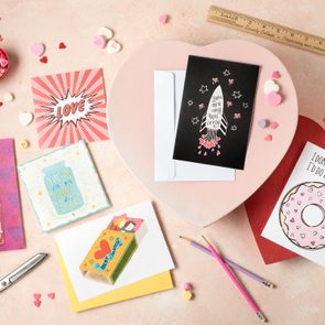 printable valentine's day cards on a light pink background surrounded by pencils, scissors, a ruler, and conversation hearts candy