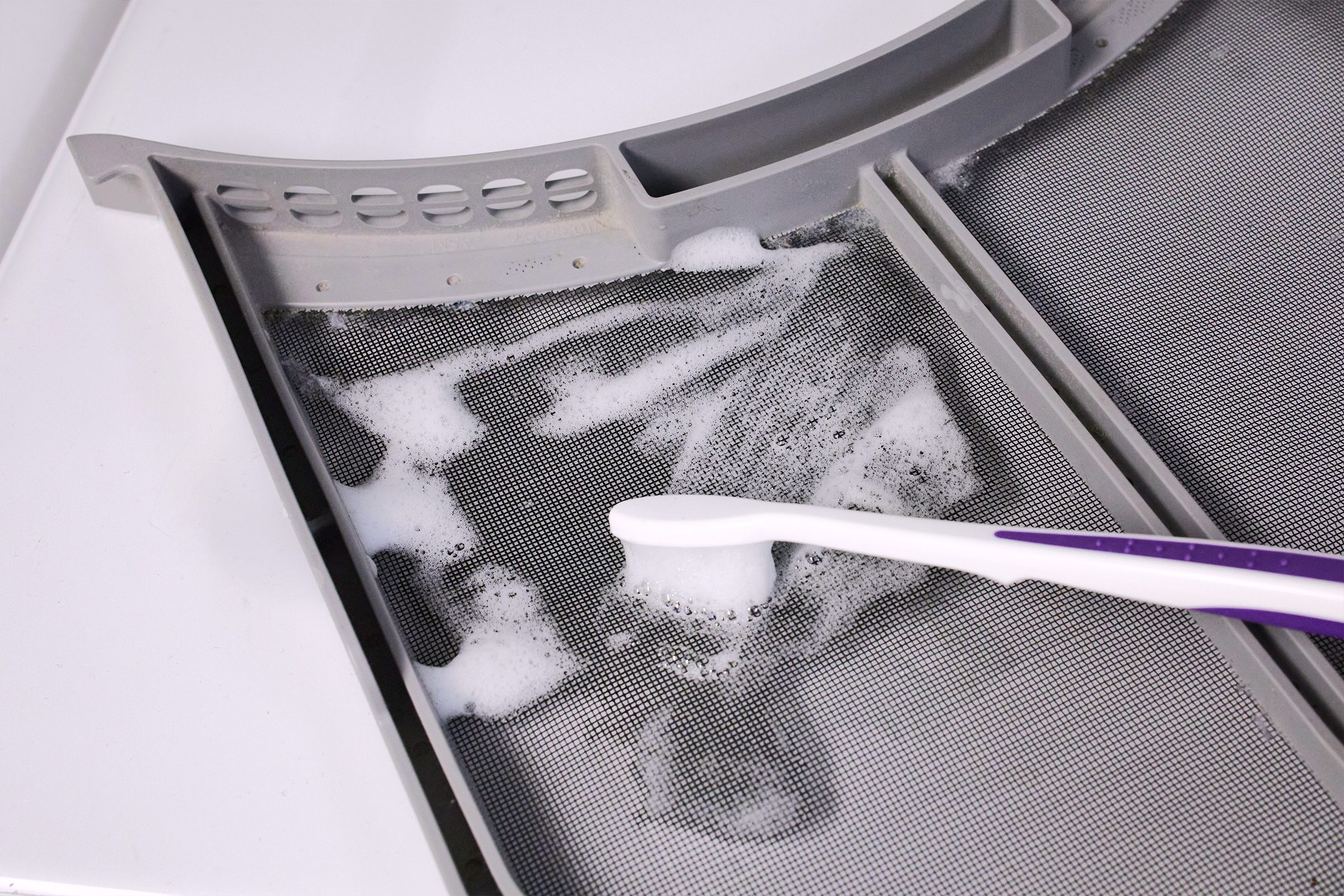 Cleaning A Dryer Lint Trap with toothbrush