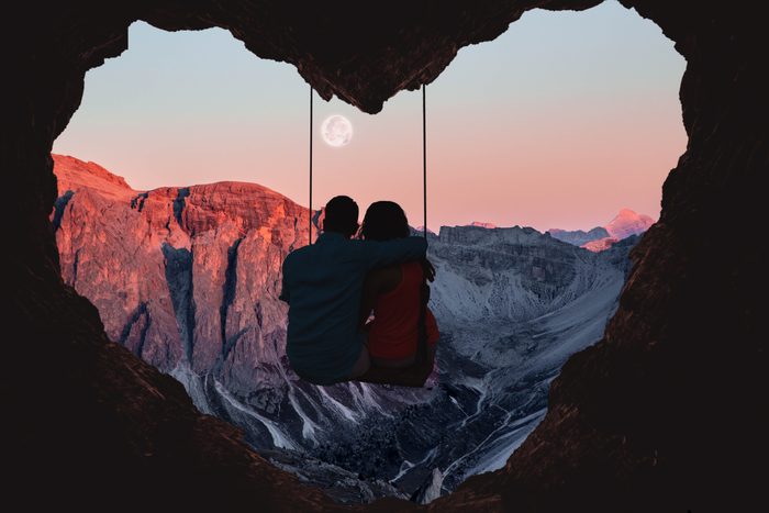 couple sitting on a swing with a scenic mountain view in the background
