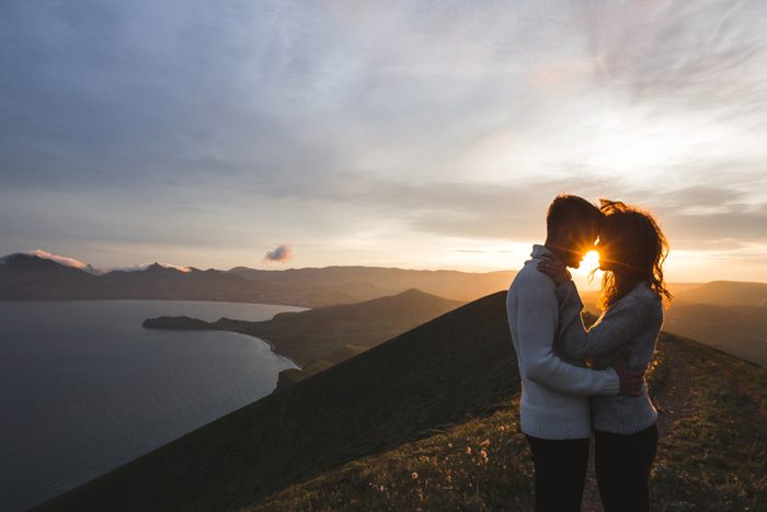 Happy couple hugging and kissing at sunset on top of a mountain