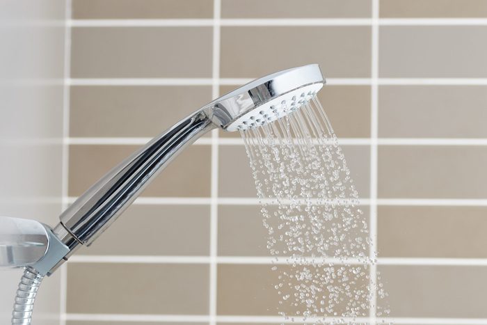 shower head with running water in front of tan tiles background