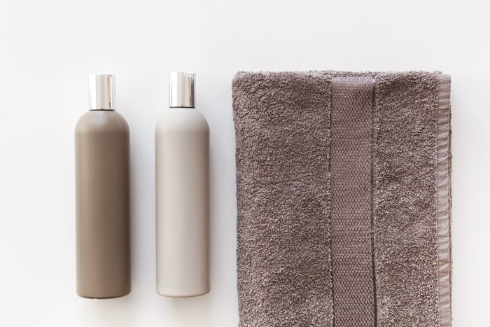 Plastic bottles of shampoo and body gel on towel isolated on white. Flat lay