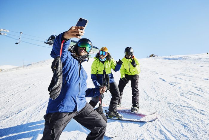 Man taking a selfie with friends at top of ski slope on sunny winter afternoon