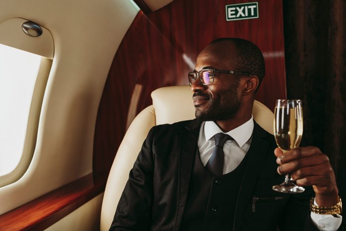 Smiling male entrepreneur holding champagne looking through window in private jet