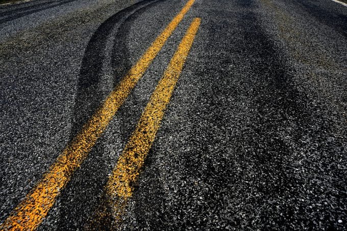 Marcas de deslizamiento que cruzan la doble línea amarilla en una carretera, evidencia de un accidente automovilístico