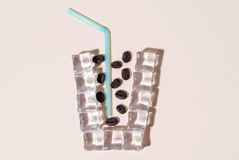 flat lay of coffee beans and a blue straw inside a cup shaped outline made with ice cubes; cold brew coffee concept