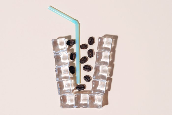 flat lay of coffee beans and a blue straw inside a cup shaped outline made with ice cubes; cold brew coffee concept