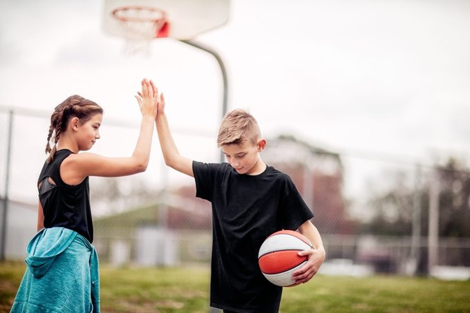 pre-teen boy and girl giving each other a high-five after basketball game