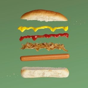 exploded view of a hot dog, relish, ketchup, mustard, bun on green background