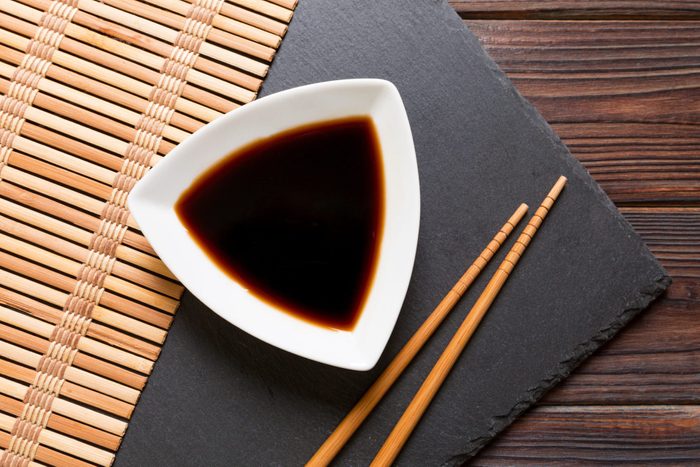 Chopsticks and soy sauce on black stone plate, wooden background