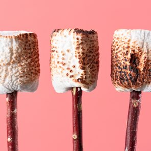 three Roasted Marshmallow on Twigs against pink background