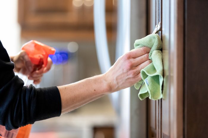 Woman Cleaning Kitchen Cabinet Handle with Disinfectant Product During Covid-19