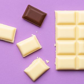 white chocolate candy bar with some pieces broken off and one piece of milk chocolate on a purple background
