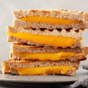 grilled cheese sandwich halves stacked and cut to reveal american cheese inside; stacked sandwich halves on gray plate against a gray background