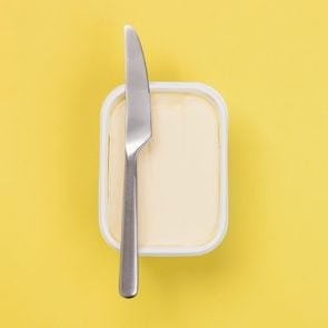 tub of margarine with a knife resting on top on a yellow background