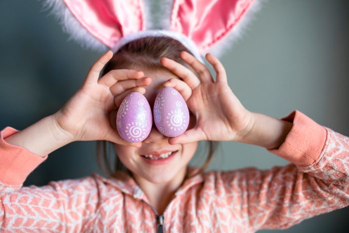 Playful girl wearing rabbit ears headband while holding Easter Eggs at home