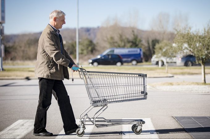 Hombre adulto mayor que empuja el carro vacío en el estacionamiento del supermercado