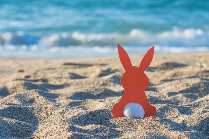 Creative easter photo of red paper bunny on the sand on the beach at sunset. Concept of Easter celebrations in tropical countries.